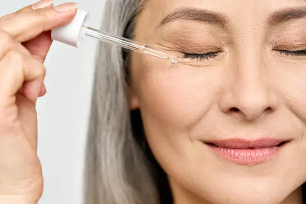 Photo of Closeup cut portrait of mature senior Asian woman with pipette serum essence.