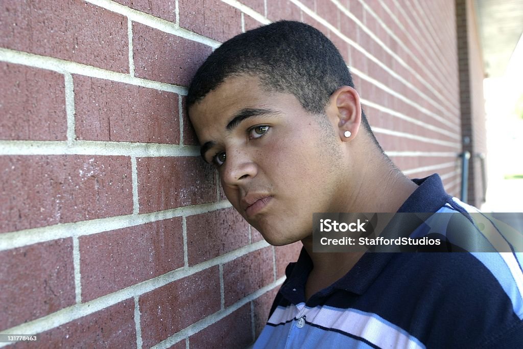 Man leaning against brick wall, looking sad Young, African American male leans his head against a brick wall with an expression of sadness. Fear Stock Photo