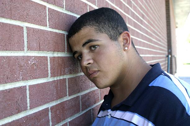 Man leaning against brick wall, looking sad stock photo