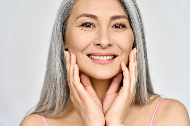 Senior happy middle aged mature asian woman closeup portrait. Skin care advertising. Closeup portrait of gorgeous happy middle aged mature asian woman, senior older 50 year lady looking at camera touching her face isolated on white. Ads of lifting anti wrinkle skin care, spa. asian beauty woman stock pictures, royalty-free photos & images