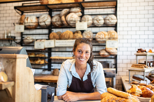 Portrait of a successful female bakery owner. Woman wearing apron leaning to the counter looking at camera.
