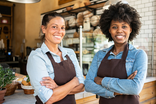 Portrait of two women wearing apron starting new coffee shop. Restaurant business partners standing together and looking at camera.