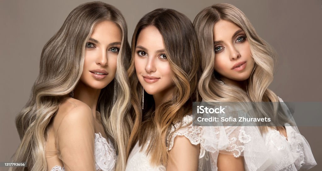 Three young attractive models  is demonstrating professionally dyed long hair. Elegance, hairstyling and makeup. Three young attractive models dressed in wedding gowns is demonstrating professionally dyed long hair. Multilayer, complex colouring of woman hair. Modern trends of hair dye. Hairstyling art. Hair Stock Photo