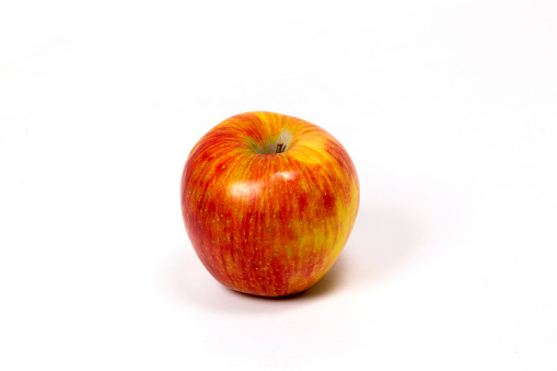 This red and yellow honey crisp apple is shot on a white seamless background. The photograph is taken from a slightly elevated angle. The fresh fruit is shiny and has hues of red and yellow. There is a short stem still on the top of the apple. There is a feint shadow cast from the round object and is a great shot for preparation cookbooks, ingredient, catalogs, chef, diet and cooking websites or magazines.