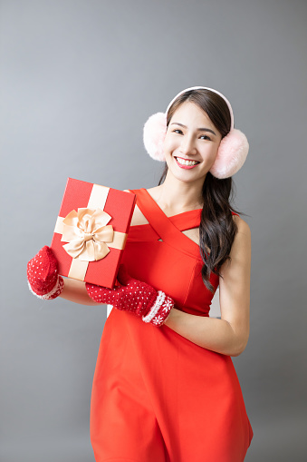 Portrait of happy beautiful young asian woman wearing christmas clothes holding gift isolated on gray background