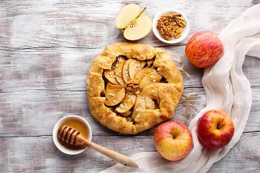 Homemade crostata pie with ripe apples, nuts and maple syrup on rustic white wooden background. Top view, copy space. Autumn holiday time concept