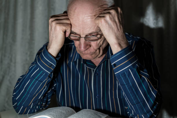 istock Senior man in glasses sitting at table and reading book at night. 1317805998
