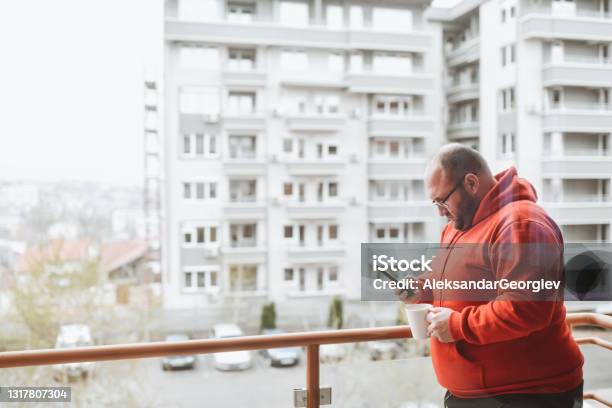 Bald Male Drinking Coffee On Balcony And Using Smartphone Stock Photo - Download Image Now