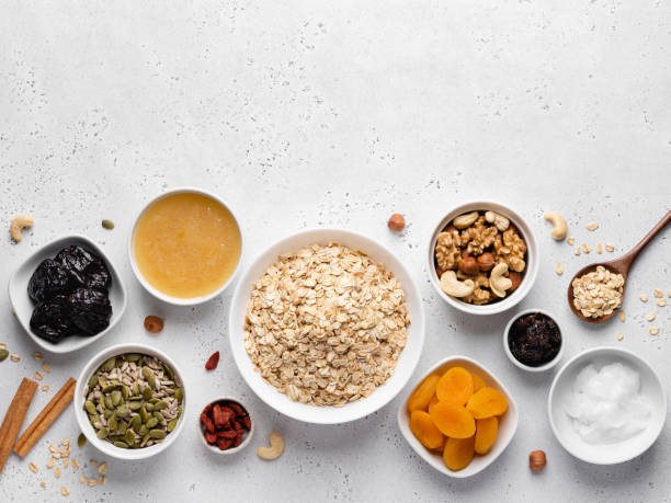 granola ingredients top view. oatmeal (flakes), nuts, seeds, prunes, dried apricots and berries, honey bowl. grey concrete background. - oatmeal rolled oats oat raw imagens e fotografias de stock