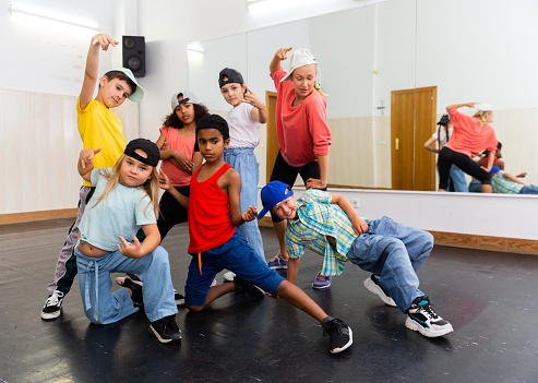 Cheerful children having fun in dance school, posing with female coach during hip-hop group class