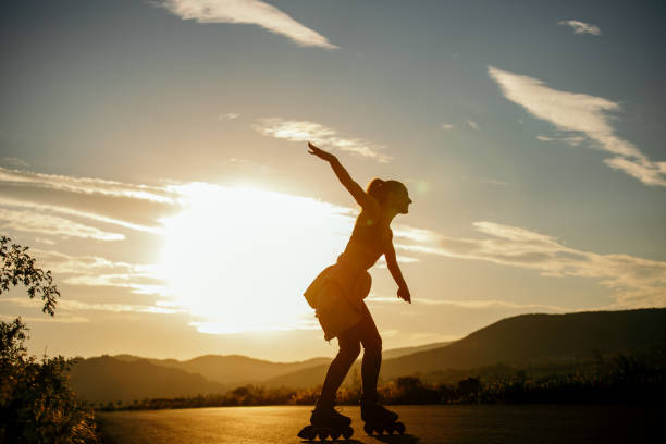 Beautiful young woman enjoying roller skating on the road in non urban area at sunset. She is beautiful and very happy