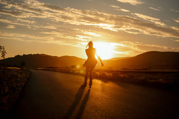 Beautiful young woman enjoying roller skating on the road in non urban area at sunset. She is beautiful and very happy