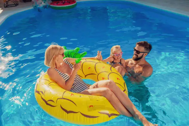 Young parents having fun playing with their daughter in the swimming pool, enjoying hot sunny summer day outdoors and relaxing while on a summer vacation