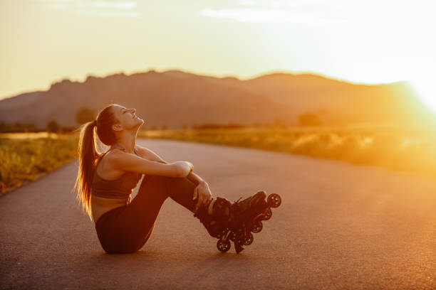Beautiful young woman enjoying roller skating on the road and relaxing in non urban area at sunset. She is beautiful and very happy