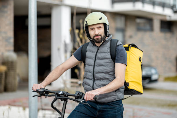 istock Delivery man in helmet with yellow backpack rides electro scooter 1317816180