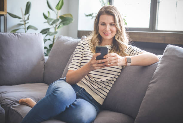 istock attractive middle aged woman sitting on the couch( mobile phone) 1317817033