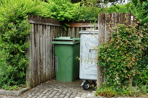 Waste separation and management. Metal container for house waste and plastic container for organic waste in a wooden niche surrounded by lush vegetation. Example of environmental  awareness.