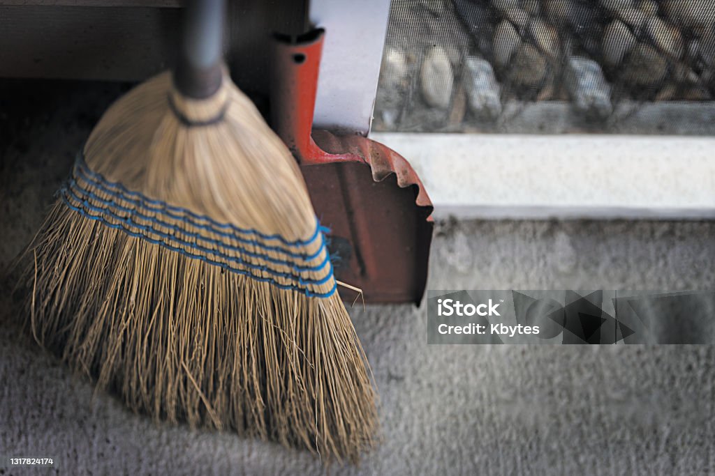 Back Porch Broom Broom and Dirty old red Dustpan on Screened Back Porch, rock garden background. Broom Stock Photo
