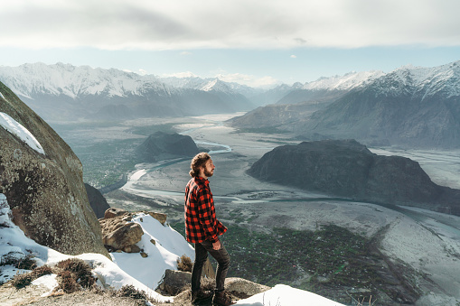 Young Caucasian man  standing on the edge of hanging rock above the river in Northern Pakistan