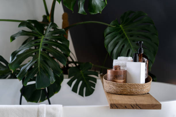 Body care products at wooden shelf on bath Wooden shelf for beauty and body care products at wooden shelf over modern white bathtub. Cozy boho style bathroom decorated with green tropical plant Monstera deliciosa bathtub photos stock pictures, royalty-free photos & images