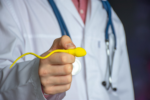 Sperm problems as cause of male infertility concept photo. Urologist or fertility specialist holds enlarged sperm model in his outstretched hand, pointing to spermogram and showing patient cause