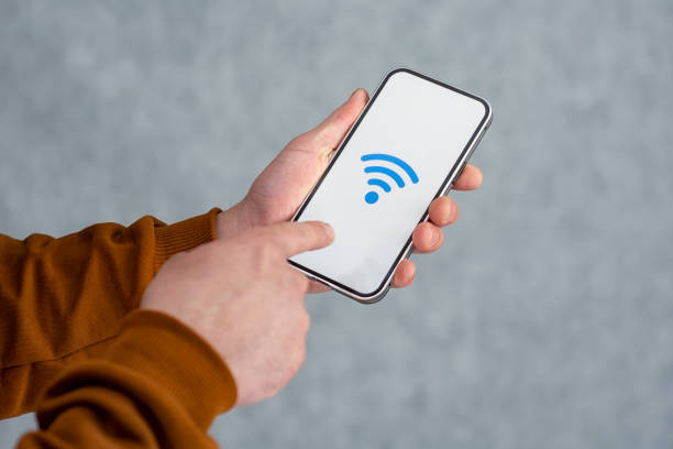 istock Man hand holding silver smartphone isolated on light background. Phone mockup with white screen and wi-fi icon. 1317839914