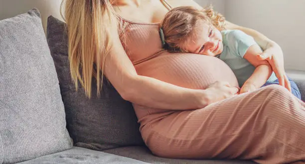 Photo of Little baby girl relaxing on mom's pregnant belly - Pregnant mother with a toddler - Family concept