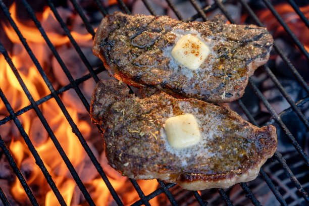 dois suculentos novos bifes de tira em uma grelha de carvão com chamas - strip steak steak barbecue grill cooked - fotografias e filmes do acervo