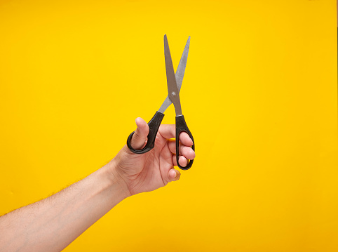 Man is showing a scissors in front of a yellow background