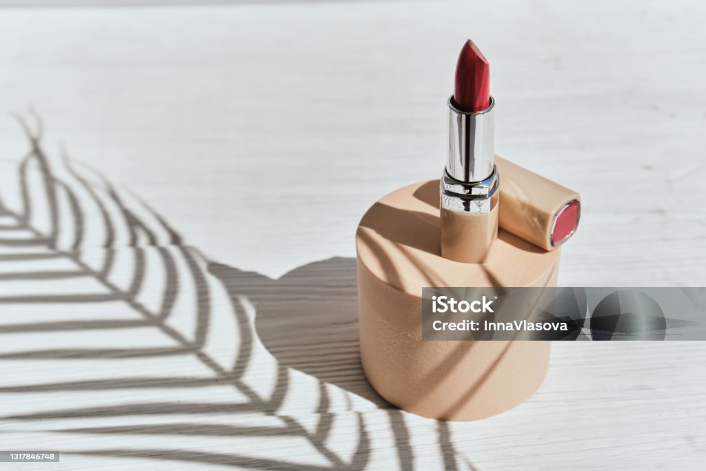 Red lipstick on a beige cylinder podium with shadows from branches of palm Red lipstick on a beige cylinder podium with shadows from branches of palm on a white background. Trend style. Mockup for the presentation of cosmetics. Lipstick Stock Photo