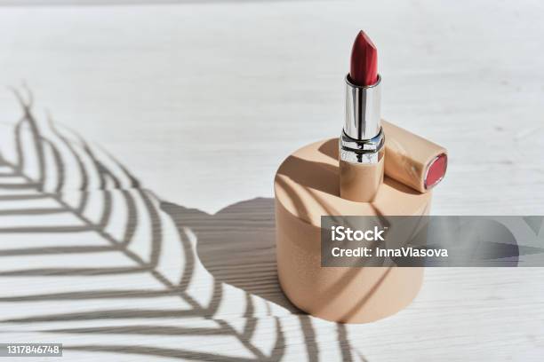 Red Lipstick On A Beige Cylinder Podium With Shadows From Branches Of Palm Stock Photo - Download Image Now