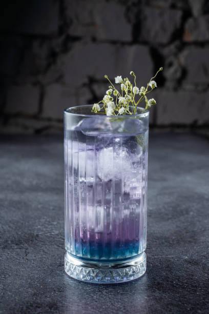 A cocktail in a tall glass with blue liqueur and ice, decorated with white flowers on gray background. A cocktail in a tall glass with blue liqueur and ice, decorated with white flowers on gray background absinthe spoon stock pictures, royalty-free photos & images