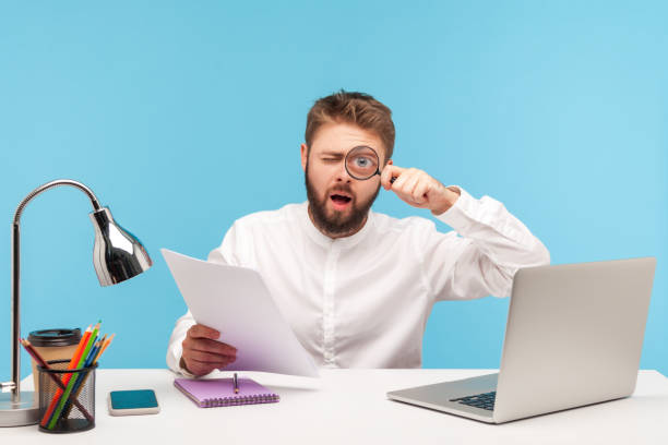 istock Attentive bearded man office worker holding loupe near eye making funny face expression, analyzing report data, working at research sitting at workplace 1317853357