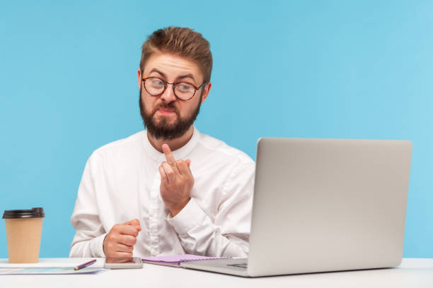 istock Miserable unkind bearded man office worker showing middle finger on laptop web camera talking video call, denial and disagreement gesture 1317853362