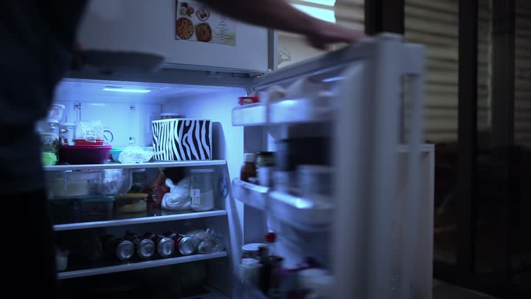 Young man openes fridge door and look inside it.