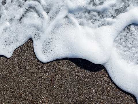 White sea foam flowing on to dark sand with dimension and texture on a summer day