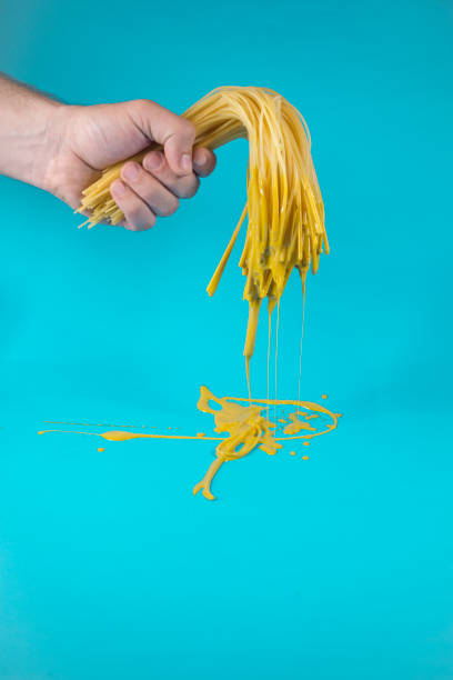 istock Hand holding half cooked spaghetti with dripping yellow paint 1317862572