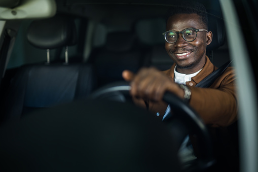 Cheerful young African American man enjoys driving his car.