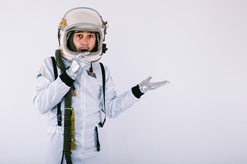 Smiling male cosmonaut in spacesuit and helmet, pointing with hand to the right, on white background.