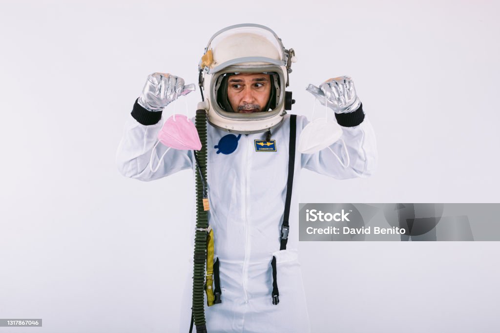 Male cosmonaut in spacesuit and helmet, holding two FPP2 masks, on white background. Covid-19 and virus concept 40-44 Years Stock Photo