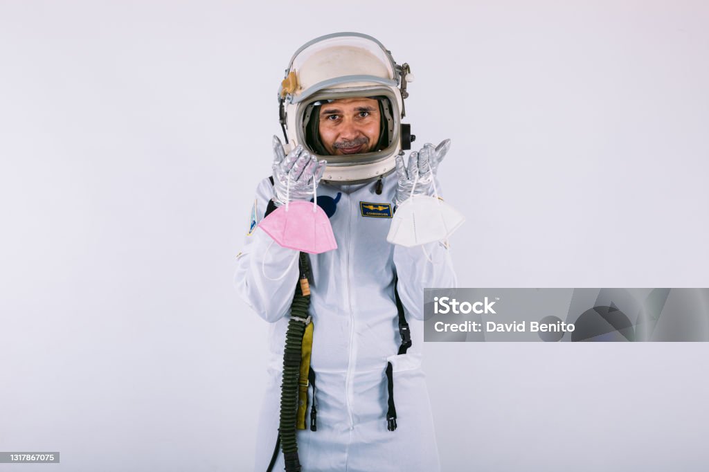 Male cosmonaut in spacesuit and helmet, holding two FPP2 masks, on white background. Covid-19 and virus concept 40-44 Years Stock Photo