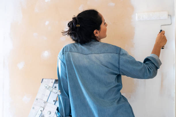 Brunette woman painting a wall on white with a paint roller stock photo