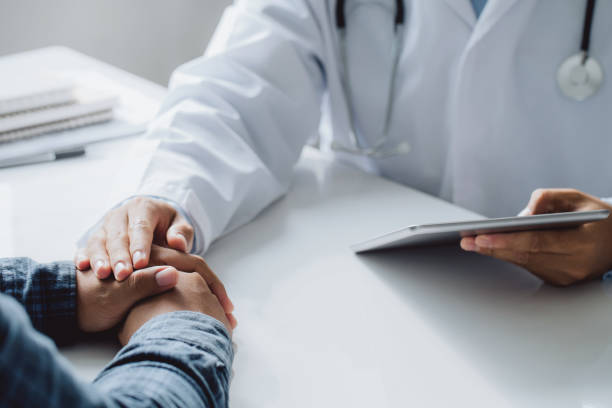 의사 격려를 위해 남성 환자의 손을 잡고 테이블에 앉아있는 동안 뭔가를 논의하는 동안 손을들고 디지털 태블릿을 들고 의사. 의학 및 건강 관리 개념. - hiv 뉴스 사진 이미지