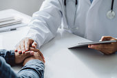 Doctor holding digital tablet while hands holding male patient's hand for encouragement and discussing something while sitting at the table . Medicine and health care concept.