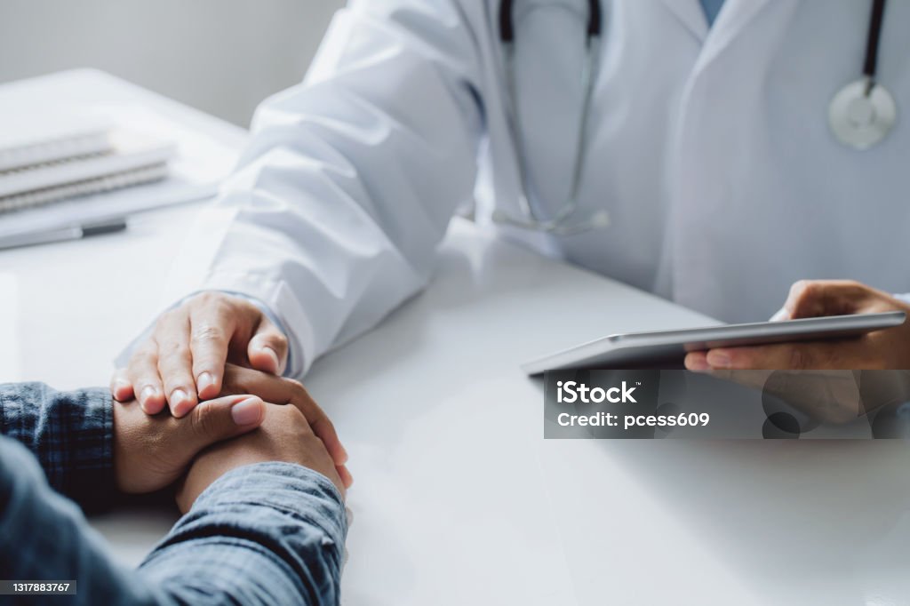 Doctor holding digital tablet while hands holding male patient's hand for encouragement and discussing something while sitting at the table . Medicine and health care concept. AIDS Stock Photo