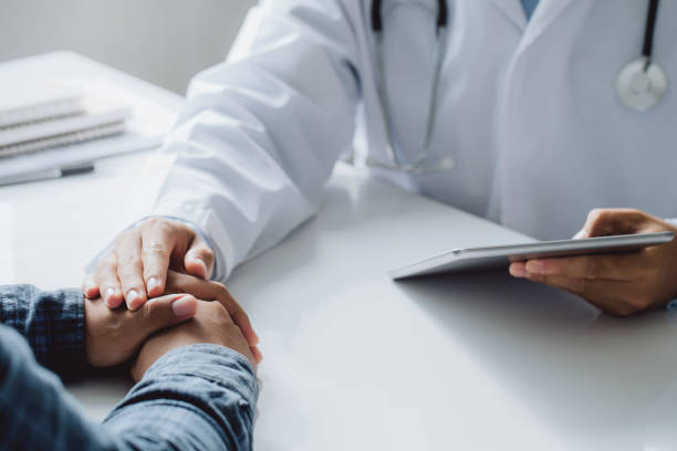 Doctor holding digital tablet while hands holding male patient's hand for encouragement and discussing something while sitting at the table . Medicine and health care concept. Doctor holding digital tablet while hands holding male patient's hand for encouragement and discussing something while sitting at the table . Medicine and health care concept. hiv stock pictures, royalty-free photos & images