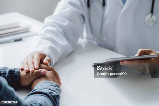 Doctor Holding Digital Tablet While Hands Holding Male Patients Hand For Encouragement And Discussing Something While Sitting At The Table Medicine And Health Care Concept Stock Photo - Download Image Now