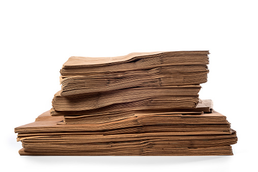 Large stack of various sizes of brown paper grocery bags sitting on a white backdrop