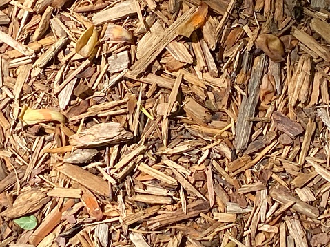 A pile of wood chips with a blue sky and a chimney in the background. Solid fuel for stoves from coniferous bark.