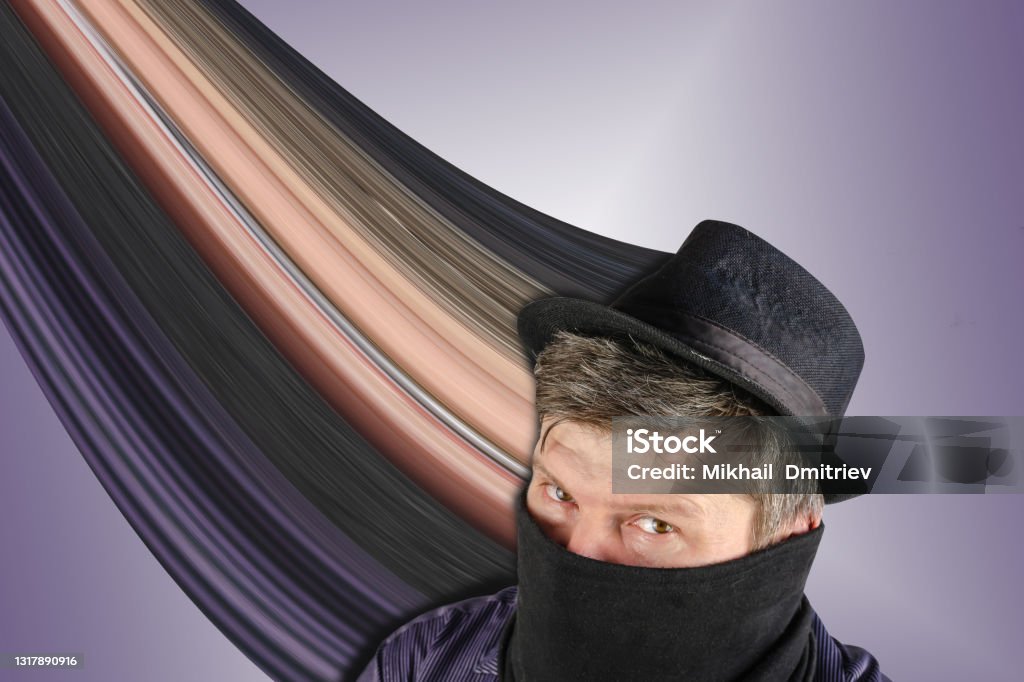 Middle-aged man wearing black hat with small brim and scarf over his face. Middle-aged man wearing black hat with small brim and scarf over his face. Male hides his face behind the buff. Unrecognizable Person on blue background. Stretch pixel effect Pixelated Stock Photo
